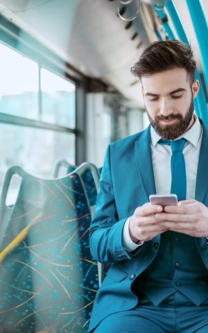 Homme en costume bleu utilisant son smartphone dans un bus, illustrant la mobilité professionnelle dans la fonction publique grâce aux aides au transport