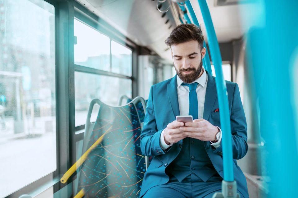 Homme en costume bleu utilisant son smartphone dans un bus, illustrant la mobilité professionnelle dans la fonction publique grâce aux aides au transport