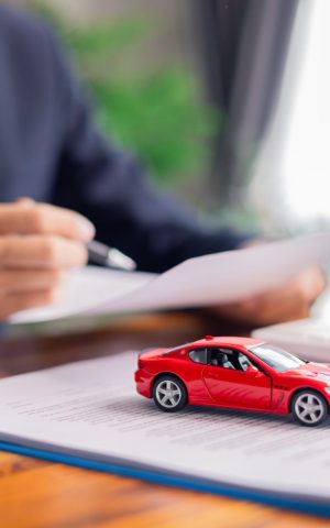 Un homme d'affaires rédigeant une politique automobile sur son bureau, avec une voiture jouet rouge.