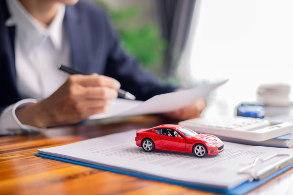 Un homme d'affaires rédigeant une politique automobile sur son bureau, avec une voiture jouet rouge.