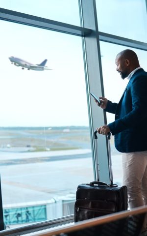 Un homme d'affaires à l'aéroport avec une valise, regardant son téléphone.