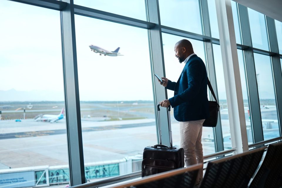 Un homme d'affaires à l'aéroport avec une valise, regardant son téléphone.