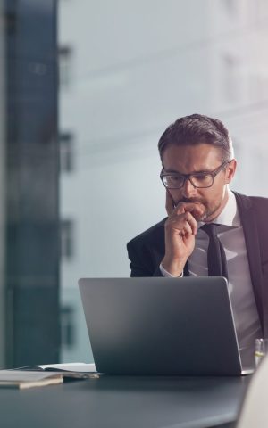 Homme en costume dans un environnement de bureau, semblant réfléchir ou se questionner.