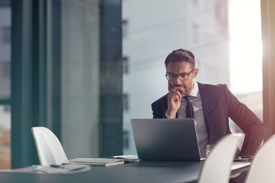 Homme en costume dans un environnement de bureau, semblant réfléchir ou se questionner.