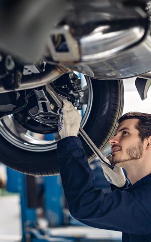 Mécanicien inspectant la suspension d'une voiture surélevée dans un atelier de réparation automobile.