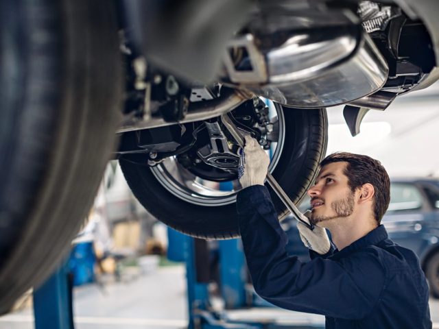 Mécanicien inspectant la suspension d'une voiture surélevée dans un atelier de réparation automobile.