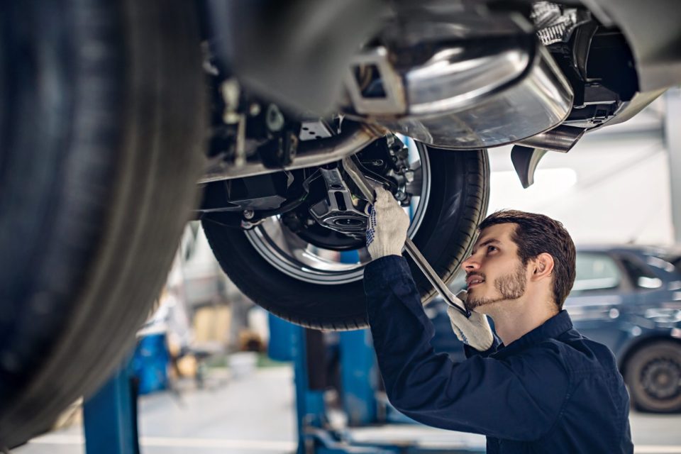 Mécanicien inspectant la suspension d'une voiture surélevée dans un atelier de réparation automobile.