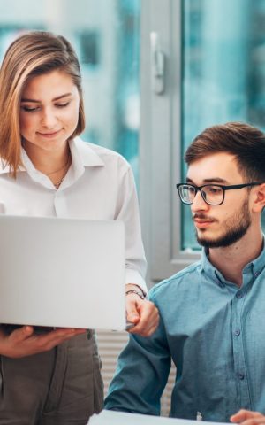 Deux stagiaires en discussion dans un bureau, travaillant sur un ordinateur portable, symbolisant les aides et droits des stagiaires en entreprise