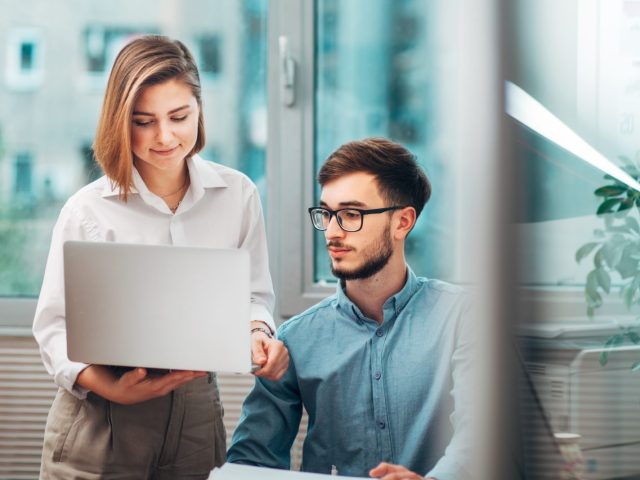 Deux stagiaires en discussion dans un bureau, travaillant sur un ordinateur portable, symbolisant les aides et droits des stagiaires en entreprise