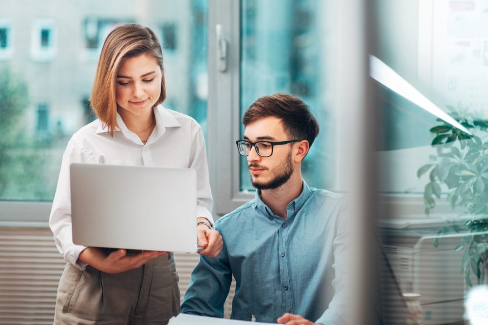 Deux stagiaires en discussion dans un bureau, travaillant sur un ordinateur portable, symbolisant les aides et droits des stagiaires en entreprise