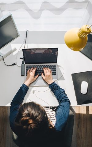 Personne travaillant sur un ordinateur portable à un bureau à domicile, avec un écran supplémentaire, une lampe jaune, et divers accessoires de bureau.