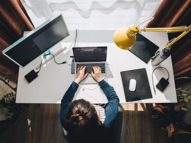 Personne travaillant sur un ordinateur portable à un bureau à domicile, avec un écran supplémentaire, une lampe jaune, et divers accessoires de bureau.