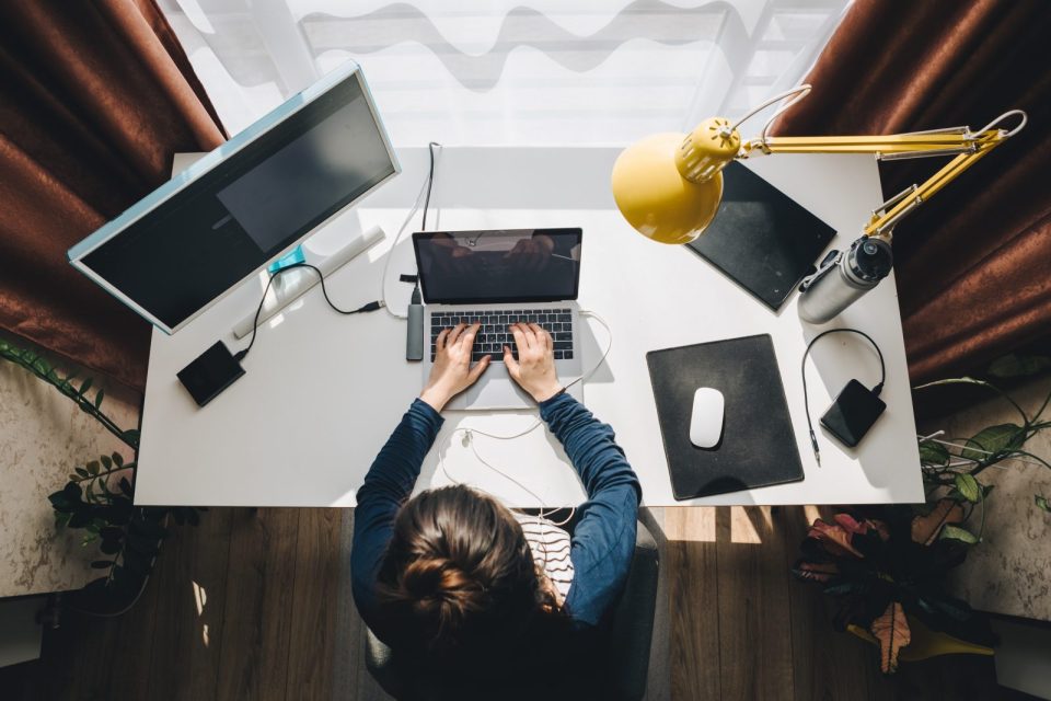 Personne travaillant sur un ordinateur portable à un bureau à domicile, avec un écran supplémentaire, une lampe jaune, et divers accessoires de bureau.