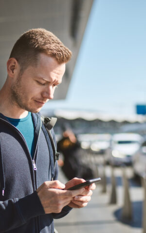 Un homme cherche un taxi sur son téléphone portable à la sortie de l'aéroport.