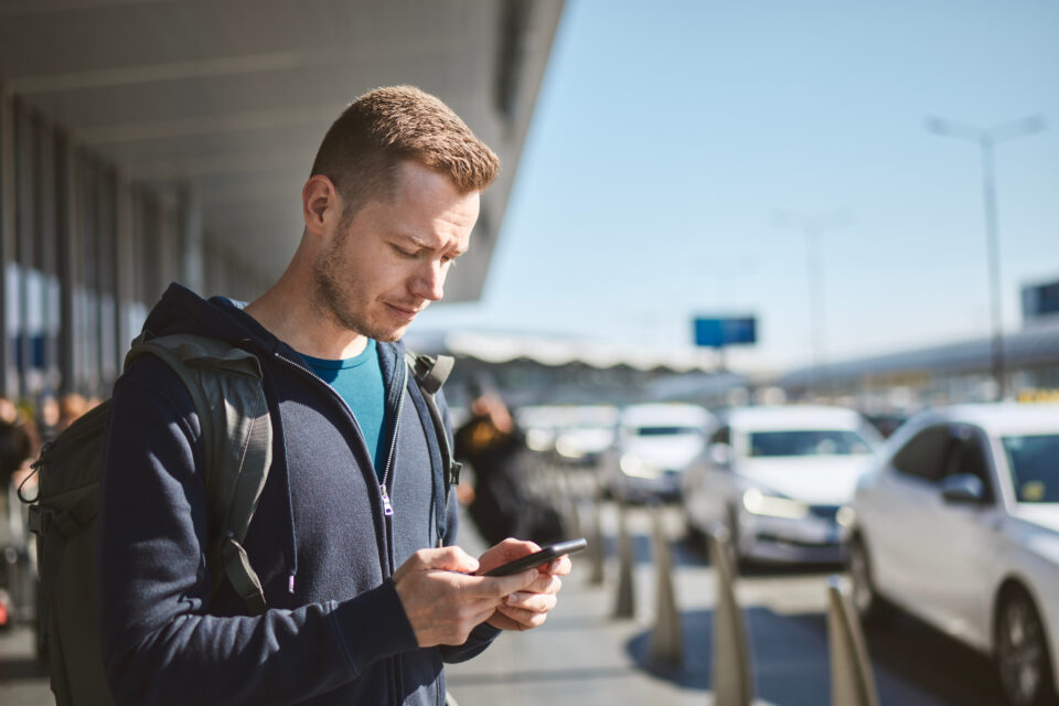 Un homme cherche un taxi sur son téléphone portable à la sortie de l'aéroport.
