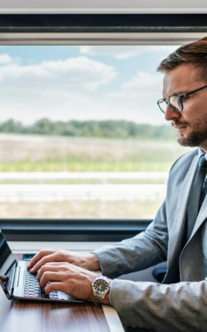 Un voyageur en costume d'affaires se déplaçant en train tout en continuant de travailler sur son ordinateur.