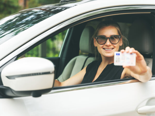 Illustration d'une femme souriante au volant de sa voiture, tenant son permis de conduire, symbolisant la réforme du permis de conduire et ses implications positives pour les conducteurs.