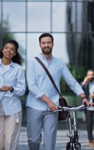 Deux adultes marchant dans la rue, l'un avec un vélo et l'autre en trottinette, symbolisant la mobilité durable en entreprise